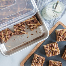 Nordic Ware aluminum rectangular baking pan with clear lid, containing chocolate pecan bars cut into squares