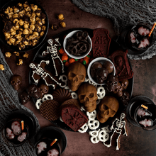 Halloween dessert charcuterie board with tombstone cakelets, skeleton cookies, chocolate treats, and candy on dark wooden surface