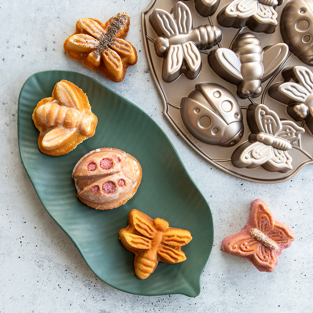 Nordic Ware aluminum Backyard Bugs baking pan with decorated insect-shaped cakes on green leaf plate