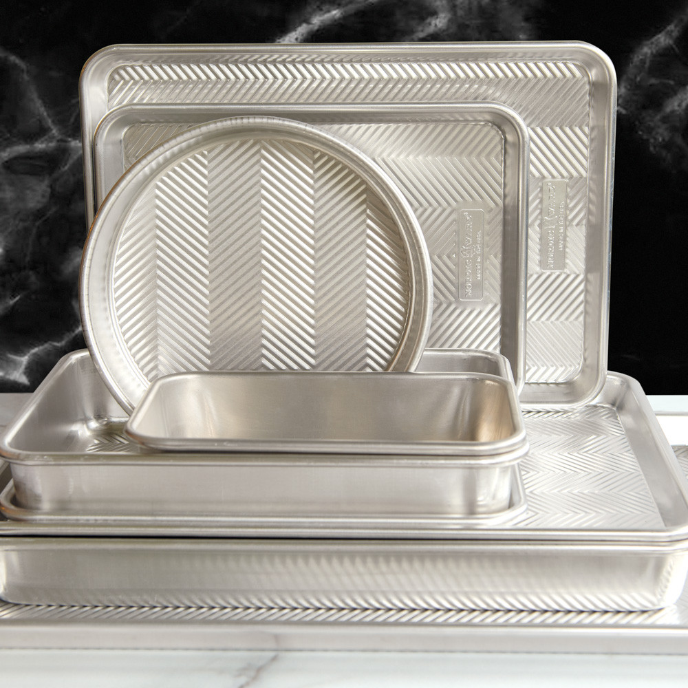 Nordic Ware Prism bakeware set stacked on marble, featuring textured aluminum pans in various shapes and sizes