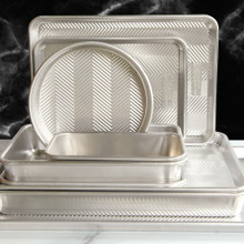 Nordic Ware Prism bakeware set stacked on marble, featuring textured aluminum pans in various shapes and sizes