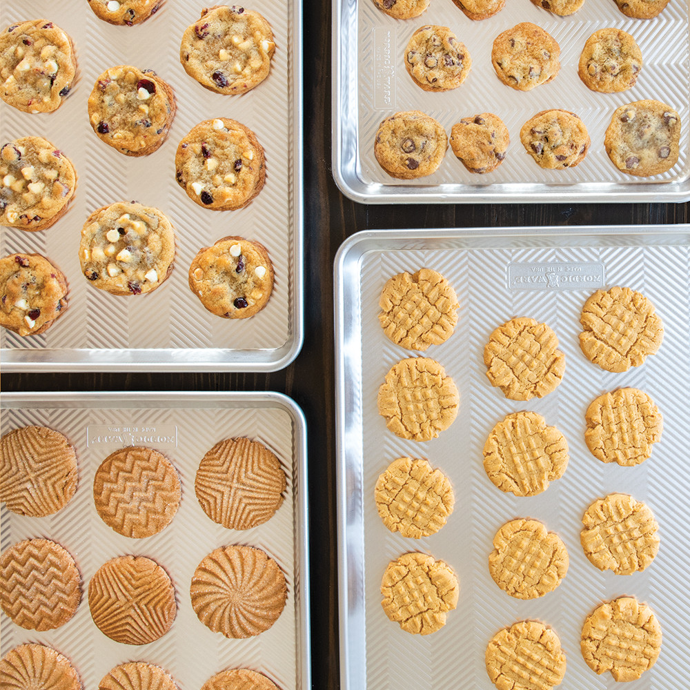 Four Nordic Ware aluminum Prism sheet pans with golden baked cookies, showing textured non-stick surfaces