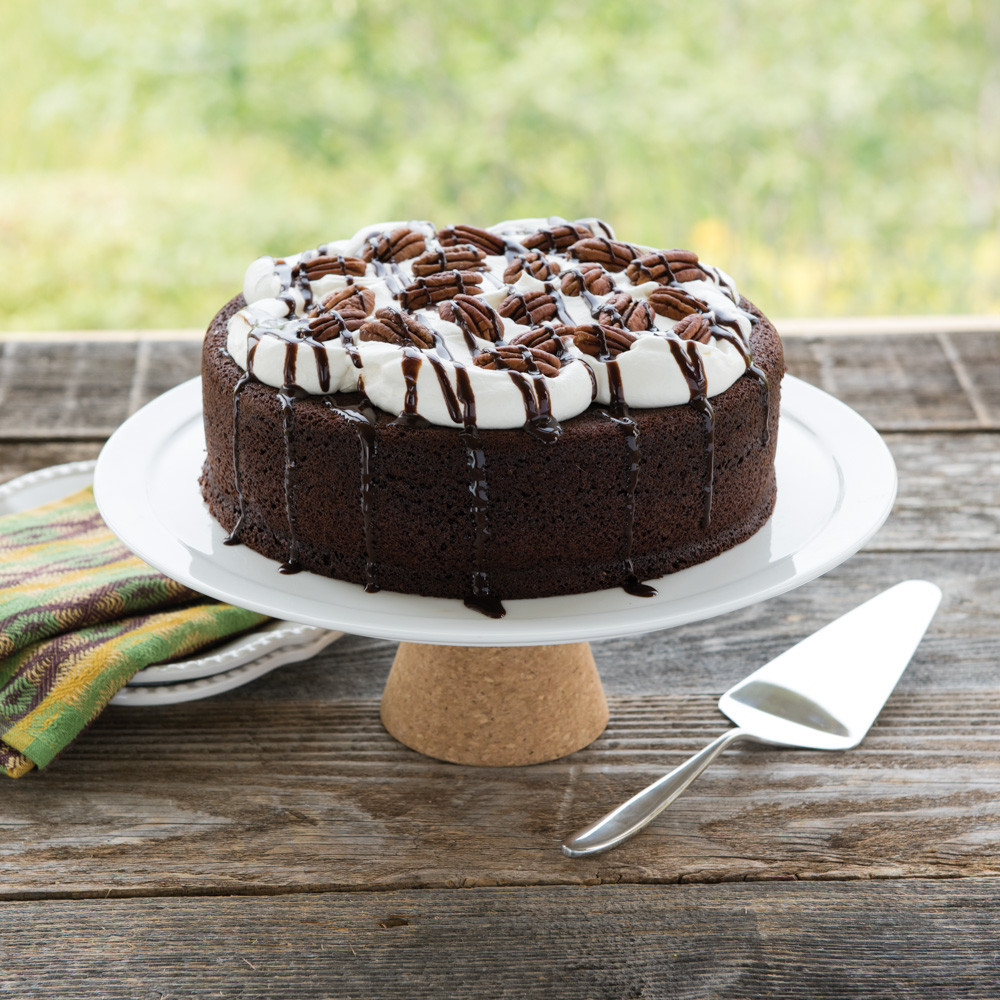 Chocolate layer cake with white frosting and chocolate drizzle on cake stand, baked in Nordic Ware round pan