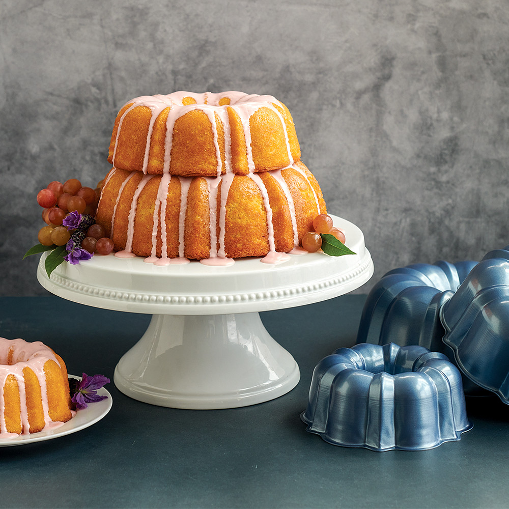 Two-tier glazed bundt cake on white pedestal with Nordic Ware aluminum bundt pans, graduated sizes