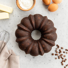 Dark chocolate bundt cake with fluted ridges surrounded by baking ingredients including flour, butter, eggs, and chocolate chips