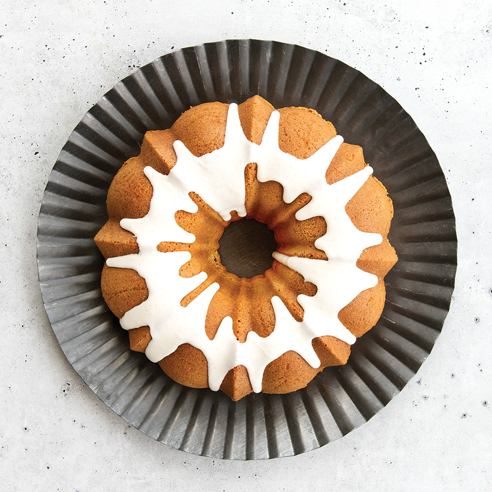 Golden vanilla bean bundt cake with white glaze on fluted gray plate, showing detailed ridged pattern