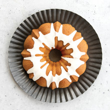 Golden vanilla bean bundt cake with white glaze on fluted gray plate, showing detailed ridged pattern