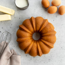 Golden vanilla bean bundt cake with fluted design surrounded by baking ingredients including eggs, butter, and milk