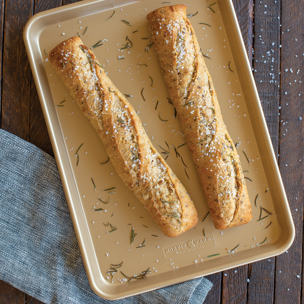 Two golden baguettes with herbs on Nordic Ware nonstick jelly roll pan, rectangular aluminum with raised edges