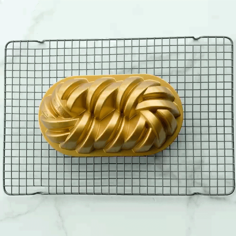 Golden bundt cake with spiral design cooling on Nordic Ware large gray wire cooling grid