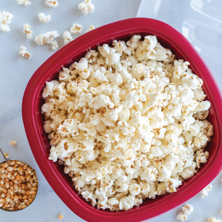 Nordic Ware red Pro Pop Popper bowl filled with freshly popped white and yellow popcorn kernels