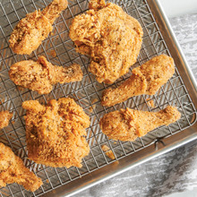 Golden fried chicken pieces cooling on wire grid in Nordic Ware aluminum sheet pan, crispy coating