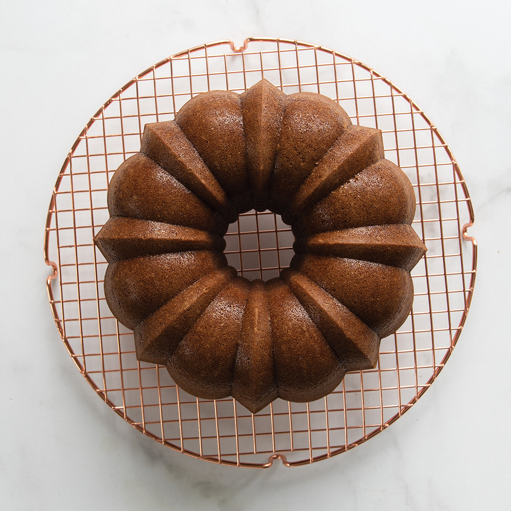 Golden brown bundt cake on Nordic Ware round copper cooling grid, overhead view on marble surface