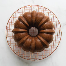 Golden brown bundt cake on Nordic Ware round copper cooling grid, overhead view on marble surface