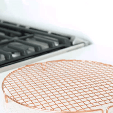 Nordic Ware round copper cooling grid with crosshatch wire pattern, positioned near stovetop