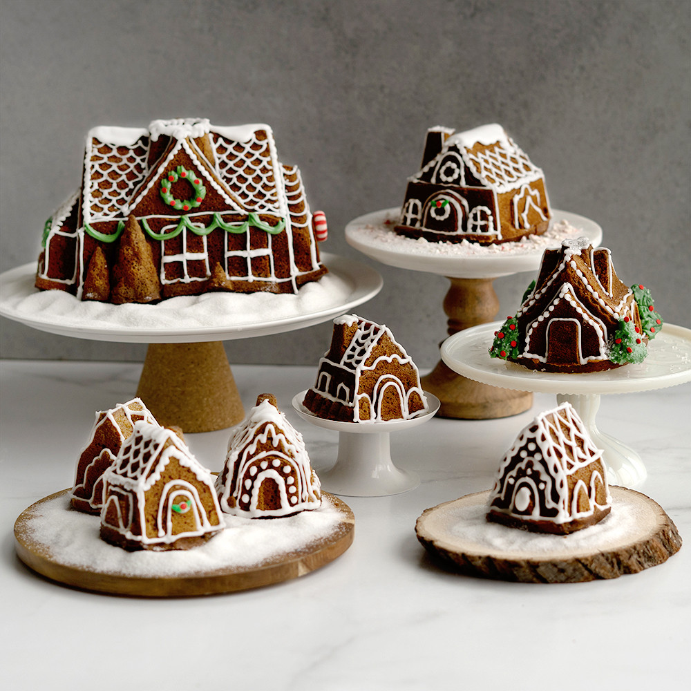 Decorated gingerbread house cakes in multiple sizes from Nordic Ware Cozy Village pans, arranged on wooden cake stands