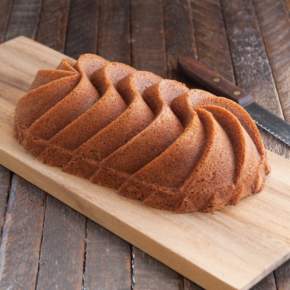 Golden vanilla loaf cake with decorative ridged pattern, sliced on wooden cutting board