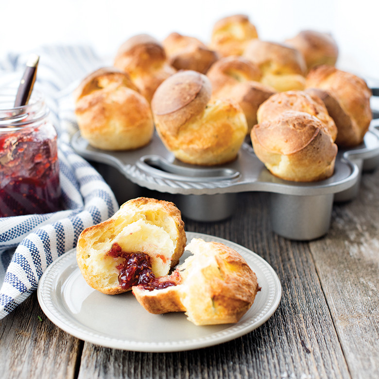 Golden baked popovers in Nordic Ware aluminum petite popover pan, one served on plate with red jam