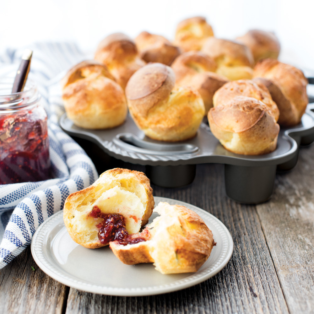 Golden baked popovers in Nordic Ware aluminum petite popover pan, one served on plate with red jam