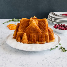 Golden bundt cake from Nordic Ware Gingerbread House pan on white plate, showing house-shaped design with detailed architectural features