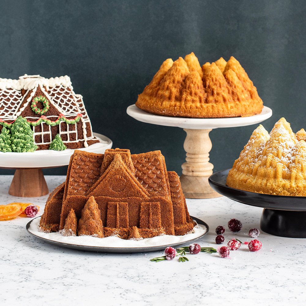 Two bundt cakes: detailed gingerbread house design and fluted pine forest pattern, both golden brown and fully baked