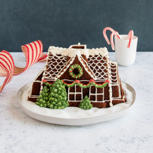 Golden bundt cake shaped like gingerbread house with decorated icing details, displayed on white plate with candy canes
