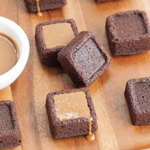 Six golden brown brownie bites baked in Nordic Ware pan, some topped with caramel drizzle, others plain