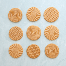 Nine golden baked cookies with geometric patterns spinning in rotation, showing detailed impressed designs from cookie stamps