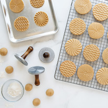 Geometric cookie stamps with baked golden cookies on cooling rack and stamped raw dough on baking sheet