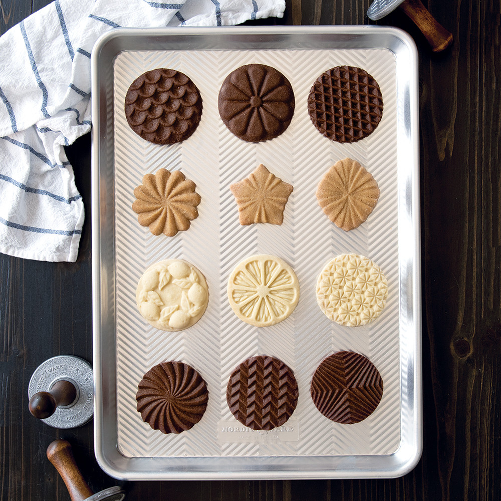 Freshly baked cookies with geometric patterns on Nordic Ware aluminum baking sheet, showcasing cookie stamp designs