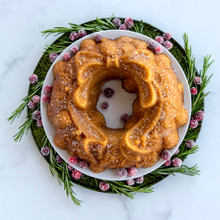 Golden baked wreath cake garnished with fresh cranberries and rosemary sprigs from Nordic Ware Holiday Wreath pan