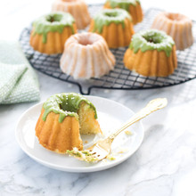 Nordic Ware Anniversary Bundtlette pan with baked mini bundt cake, aluminum with intricate fluted design