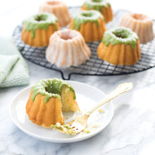 Nordic Ware Anniversary Bundtlette pan with baked mini bundt cake, aluminum with intricate fluted design