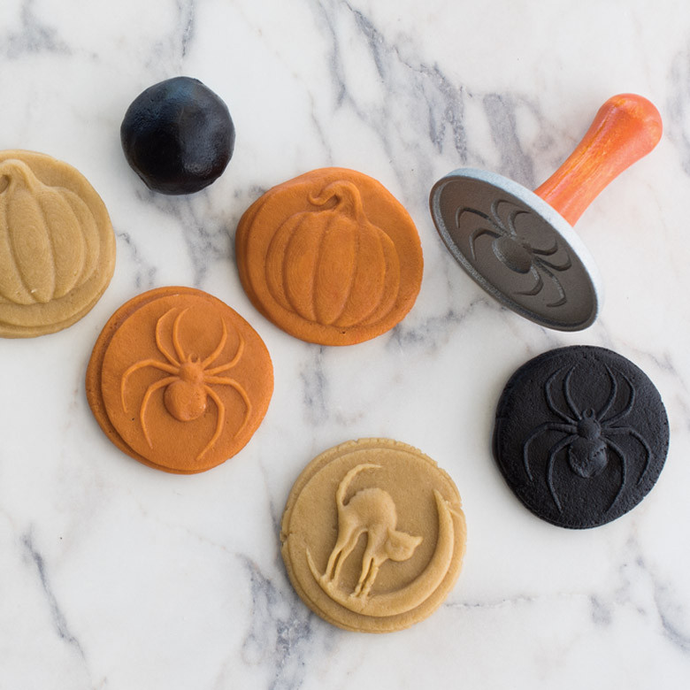 Four wooden Halloween cookie stamps with carved designs: pumpkin, witch hat, ghost, and bat on marble surface