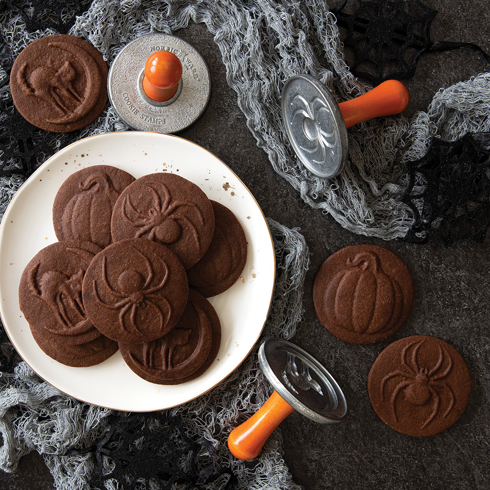 Golden baked cookies stamped with Halloween designs including pumpkins and bats, displayed on dark surface
