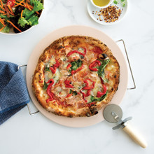 Baked pizza with golden crust on Nordic Ware stone set, pizza wheel cutter and green salad visible