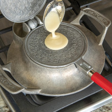 Spooning batter into center of heated Nordic Ware krumkake iron, demonstrating first step of cookie making process