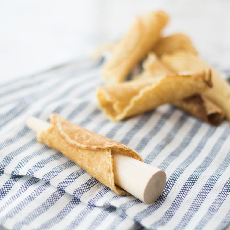 Golden krumkake cookie rolled into cone shape on striped kitchen towel, showing delicate waffle pattern texture