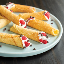 Golden cone-shaped krumkake filled with whipped cream, fresh raspberries and chocolate chips on white plate