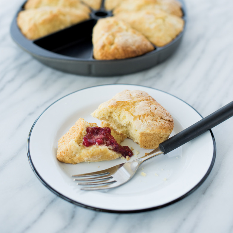 Golden baked scone wedge on white plate with red berry jam, showing triangular shape from Nordic Ware scone pan