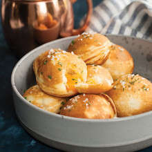 Cast iron ebelskiver pan with seven round wells, filled with golden-brown Danish pancake balls, some with melted cheese