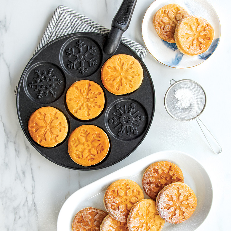 Nordic Ware aluminum snowflake pancake pan with six golden pancakes shaped like detailed snowflakes, dusted with powdered sugar