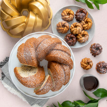 Three golden bundt cakes with braided rope pattern from Nordic Ware 75th Anniversary collection, dusted with powdered sugar