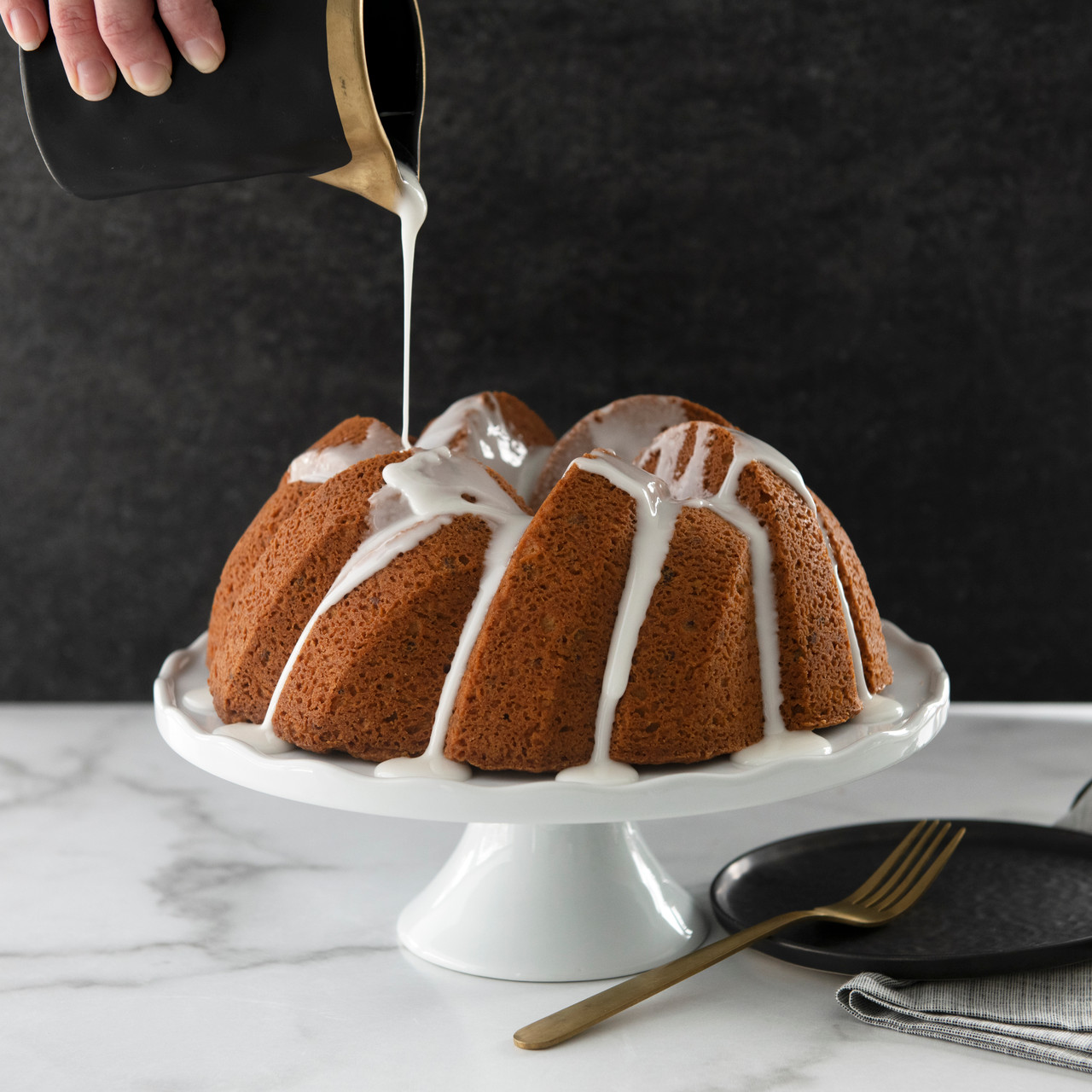 White glaze being poured over golden bundt cake in Nordic Ware 75th Anniversary Braided Bundt pan