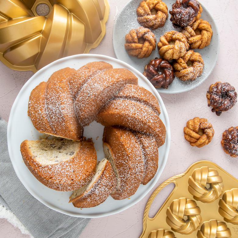 Six golden braided bundt cakes displayed with Nordic Ware aluminum mini bundt pans in background