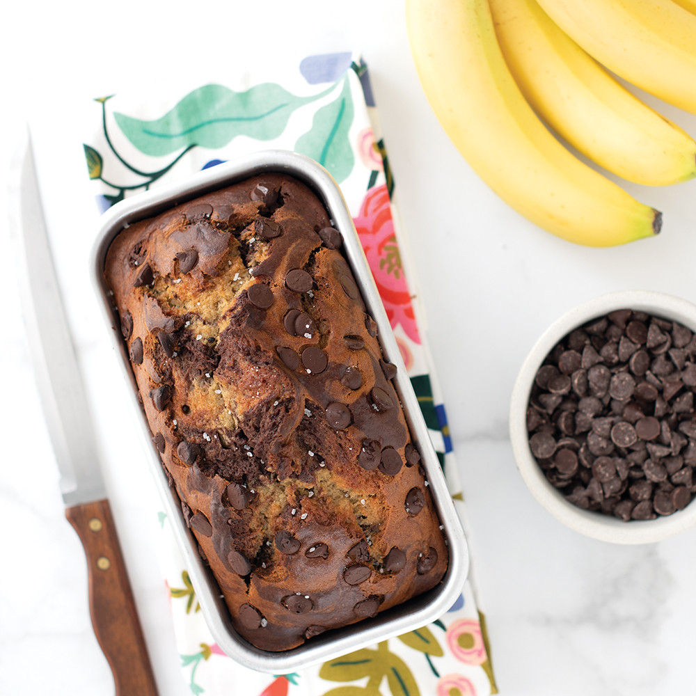 Chocolate banana bread loaf in Nordic Ware natural aluminum 1-pound loaf pan with baking ingredients nearby
