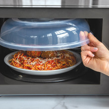Hand pulling Nordic Ware Up & Away spatter cover from microwave above plate of cooked spaghetti