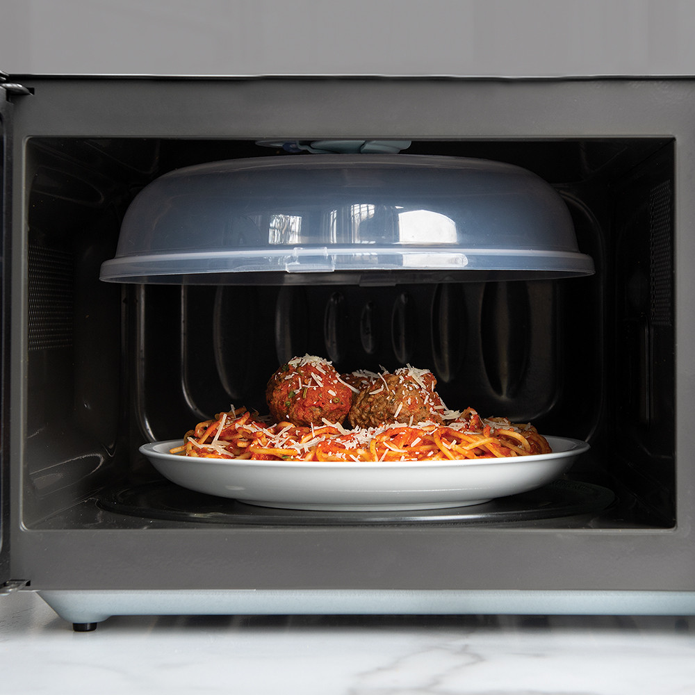 Nordic Ware Up & Away clear spatter cover stored flat against microwave interior above plate of spaghetti