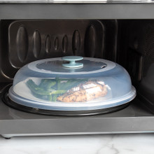 Nordic Ware clear plastic spatter cover over white plate with cooked chicken and green beans in microwave
