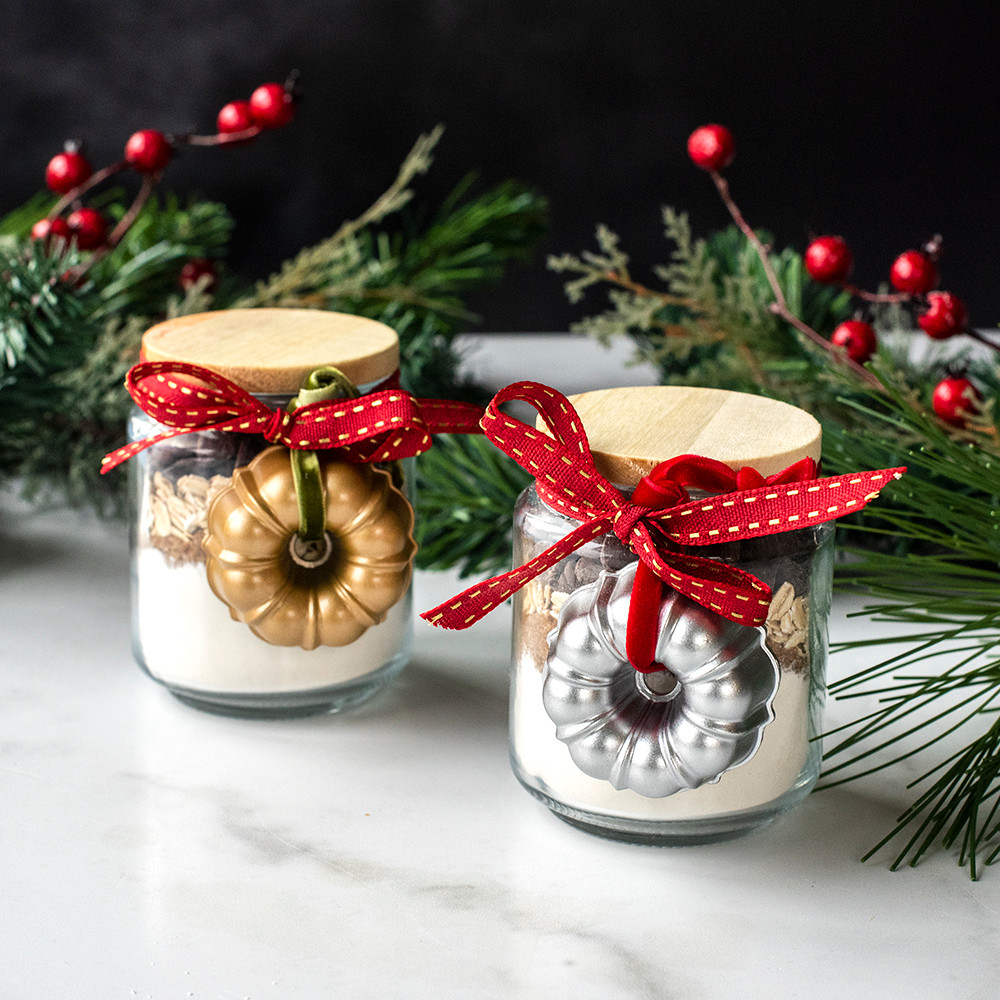 Two cast aluminum bundt ornaments, one silver and one gold, tied to glass jar filled with baking ingredients